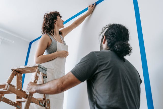 Person standing on ladder applying tape to a wall